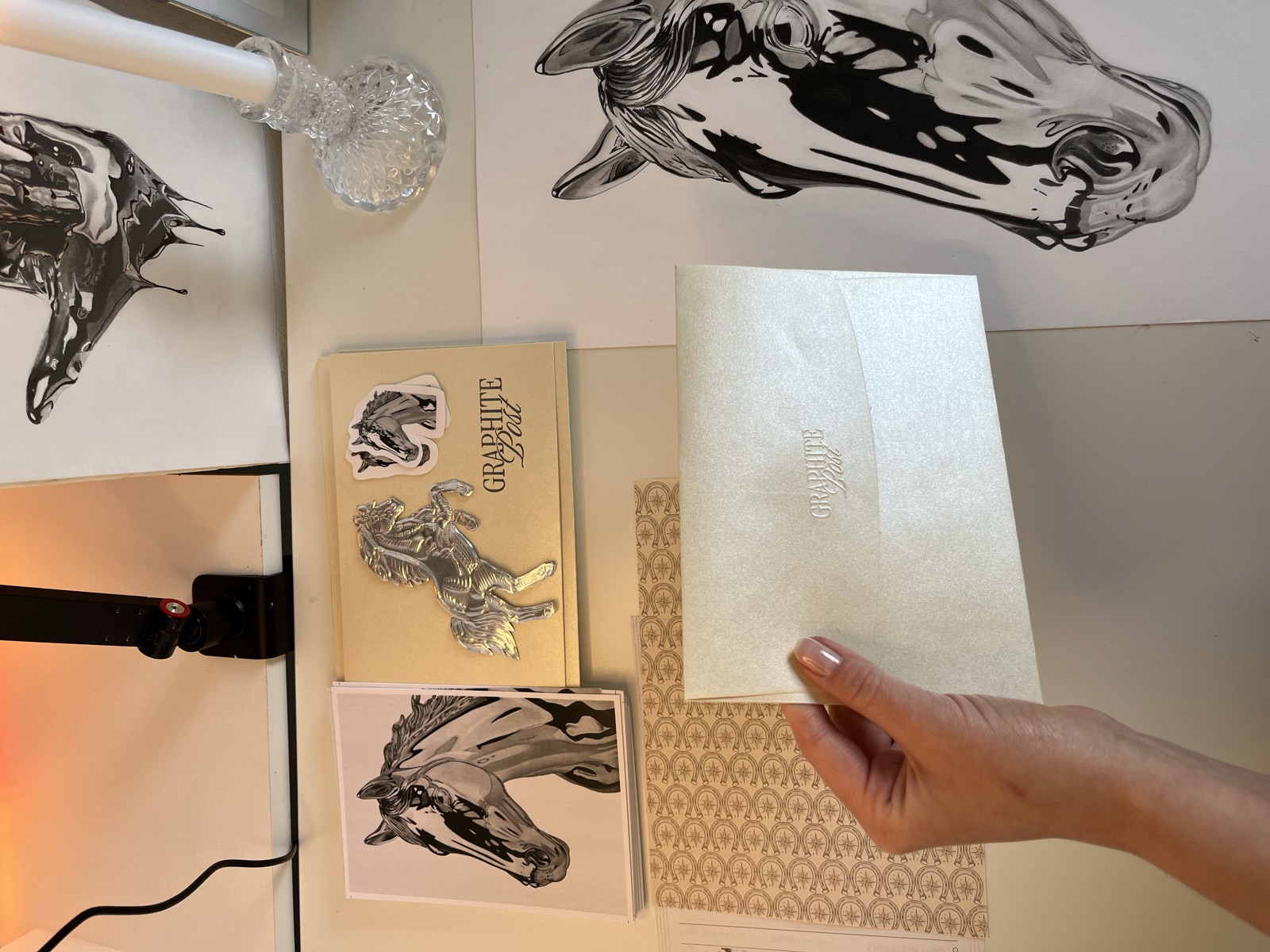 Hand holding a Graphite Post horse collection envelope with prints on desk