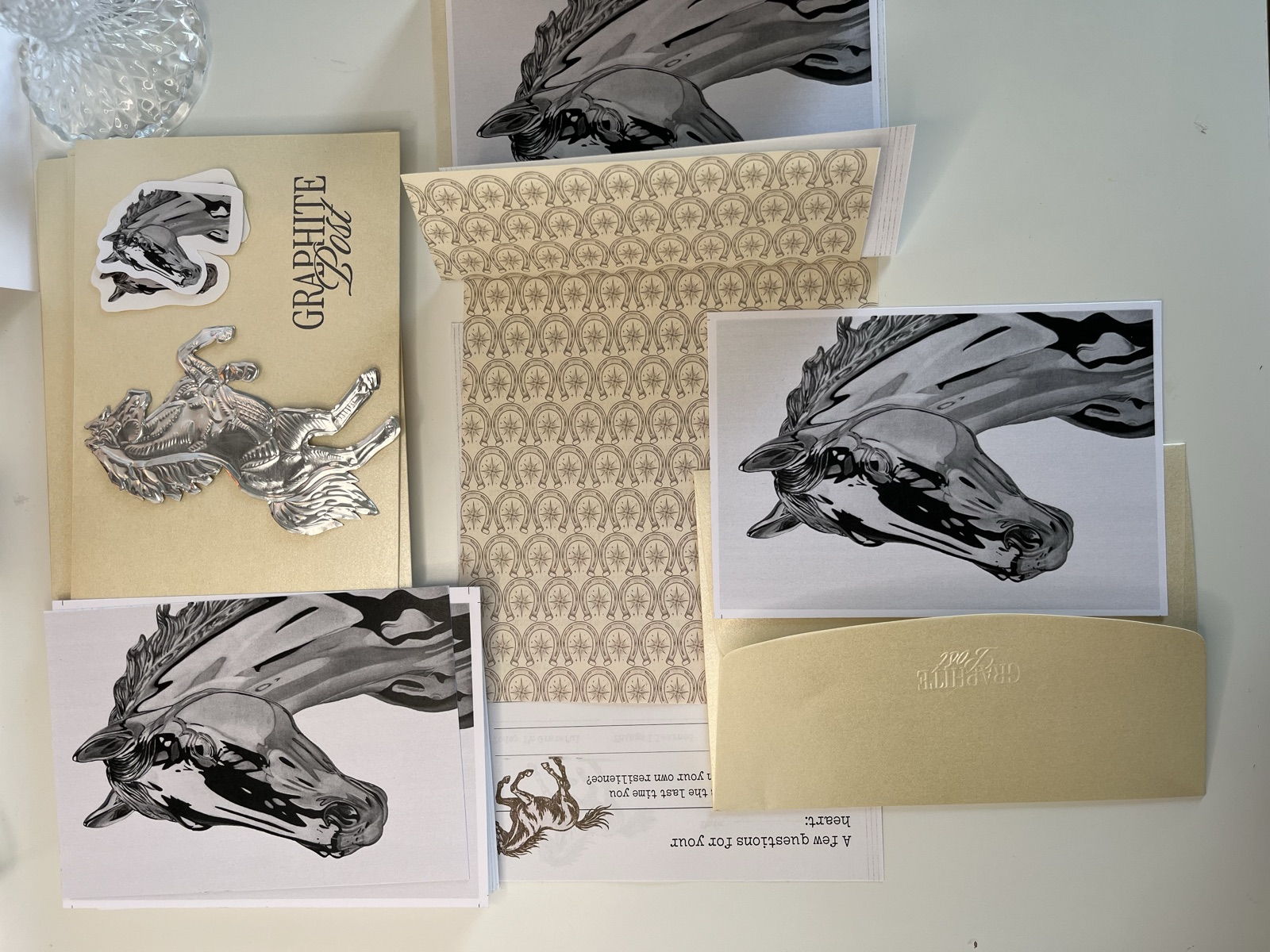Graphite Post horse collection package contents spread on table — print, bookmark, sticker and envelope