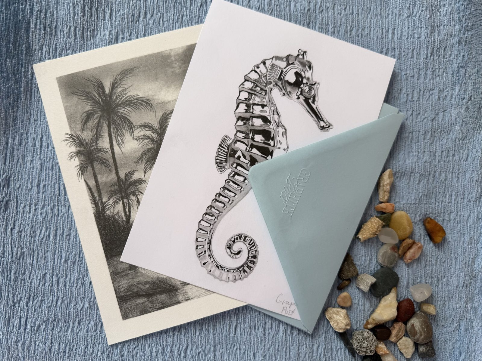 Graphite Post seahorse collection — prints and envelope on soft blue linen with beach stones